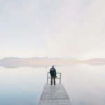 Man Wearing Jacket Standing on Wooden Docks Leading to Body of Water